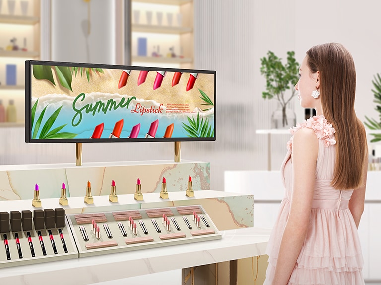 Hay una BH7N instalada en la sección de pintalabios de una luminosa tienda de cosméticos. Una mujer observa un vívido anuncio en la pantalla panorámica de la BH7N.